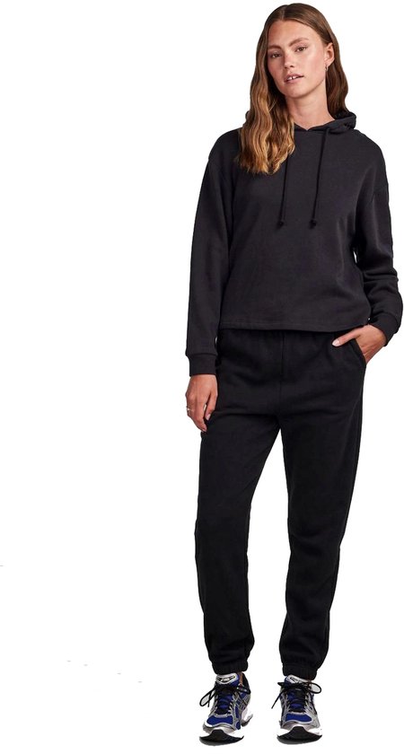 Vrouw in een zwart trainingspak met hoodie en joggingbroek.