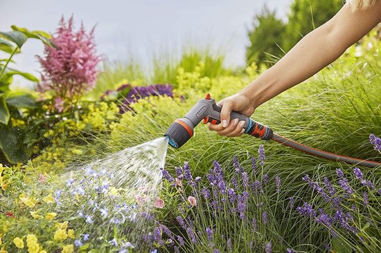 Hand met GARDENA Comfort EcoPulse spuitpistool, sproeit water op bloemen in de tuin.