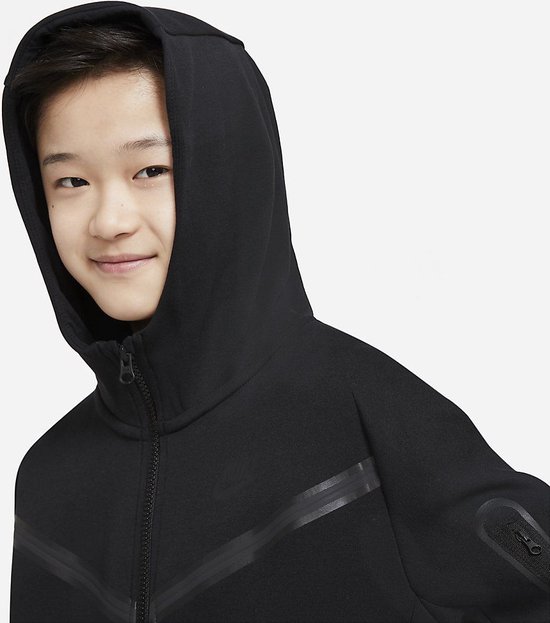 Close-up van een jongen met een zwart Nike Tech Fleece vest met capuchon op.
