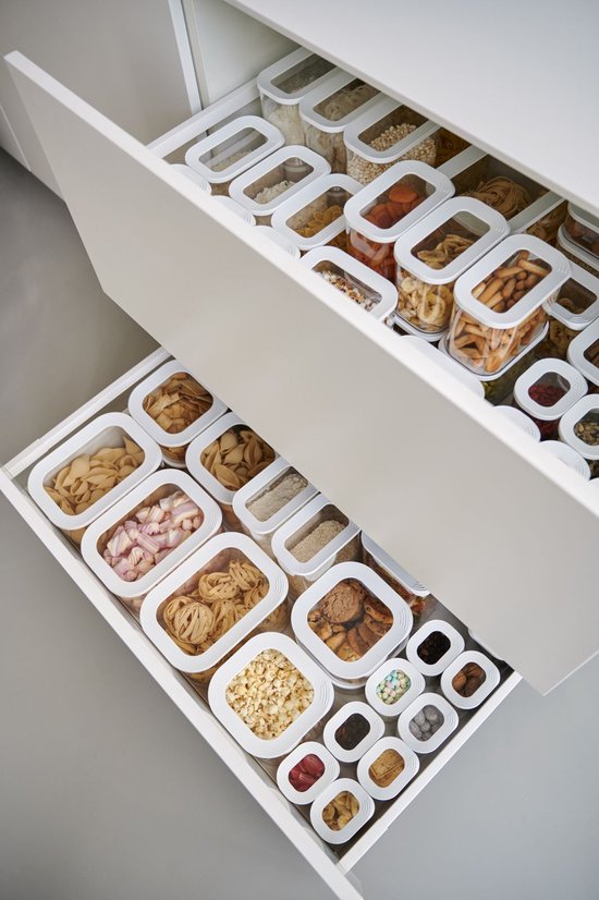 Tiroirs de cuisine avec rangement organisé, remplis de diverses boîtes de stockage avec pâtes, biscuits et muesli.