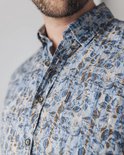 Close-up van de kraag van een man in een blauw overhemd met bruine bladprint.