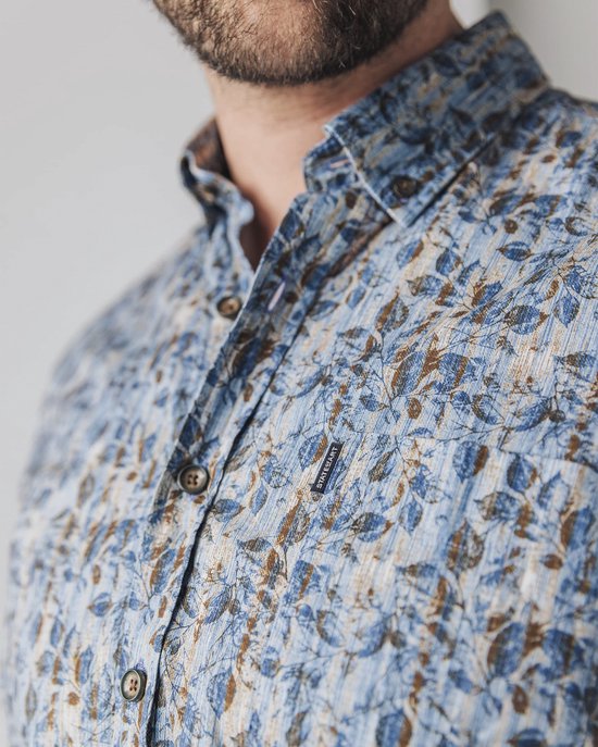 Close-up van de kraag van een man in een blauw overhemd met bruine bladprint.