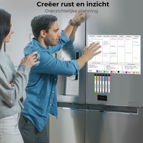 Un couple regarde un agenda hebdomadaire magnétique sur un réfrigérateur. Le calendrier est rempli de rendez-vous et d'une liste de courses.
