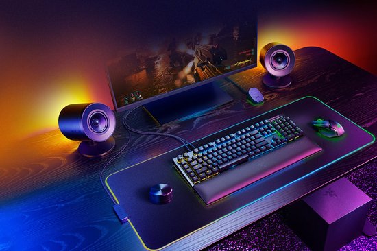 Gaming bureau met Razer speakers, toetsenbord, muis en monitor met oranje/paars licht.