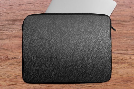 Housse pour ordinateur portable noire à texture cuir sur fond en bois, à côté d'un ordinateur portable argenté.