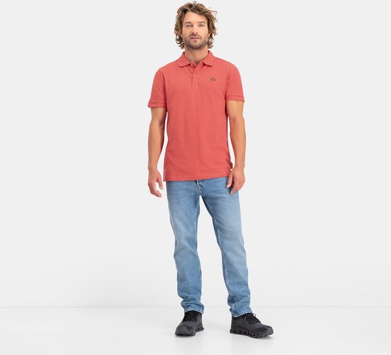 Man met steil, golvend blond haar, een rood poloshirt met korte mouwen en lichtblauwe jeans.