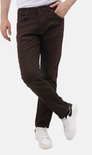 Man in bruine regular fit jeans met gekruiste benen en witte sneakers.