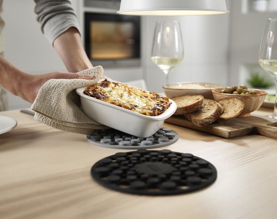 Grijze en zwarte Joseph Joseph onderzetters op een houten tafel met een ovenschotel.