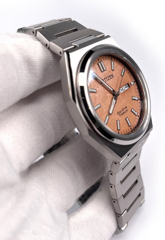Zilverkleurig titanium horloge met een perzikkleurige wijzerplaat. De kast is vierkant met afgeronde hoeken.