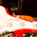 Close-up van de regelaars en de schakelaar van een rode elektrische gitaar met witte slagplaat.