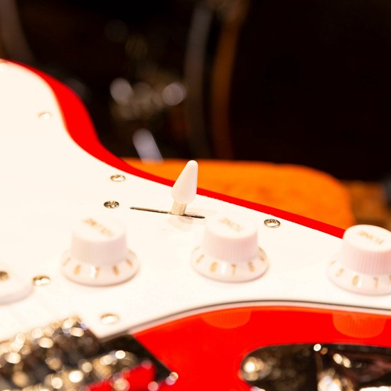 Close-up van de regelaars en de schakelaar van een rode elektrische gitaar met witte slagplaat.