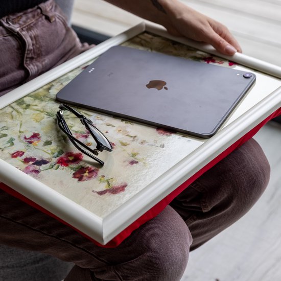 Vrouw met dienblad op schoot. Het dienblad heeft een bloemenprint van rode en witte klaprozen. Een iPad en een bril liggen erop.