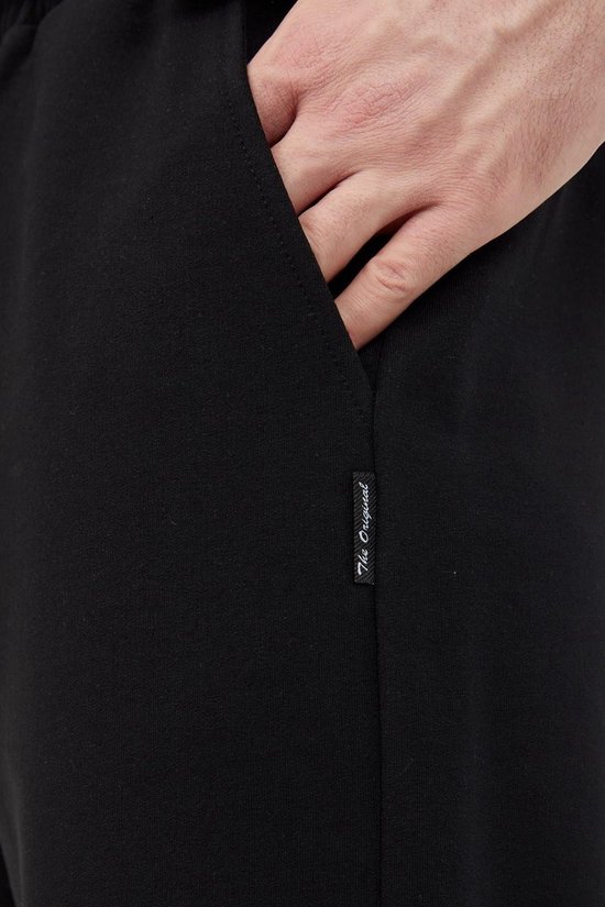Detail van een zwarte joggingbroek met label 'The Original'.
