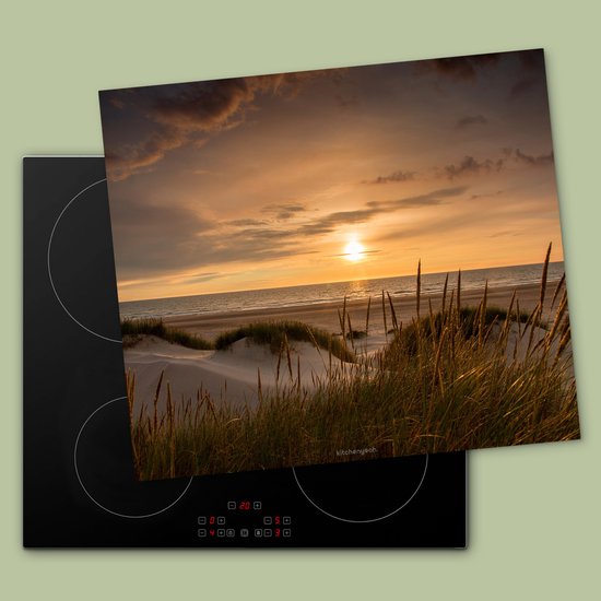 Inductiebeschermer met duinenlandschap bij zonsondergang, geplaatst op een zwarte inductiekookplaat.