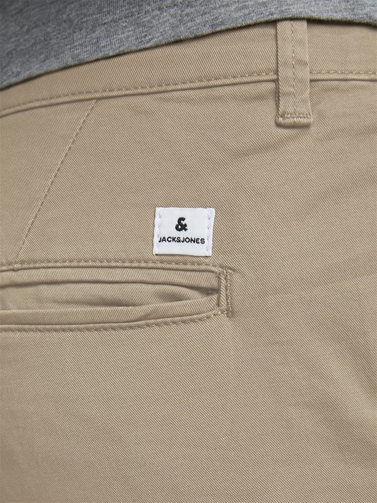 Sluiting van een beige chino broek met knoop en label.