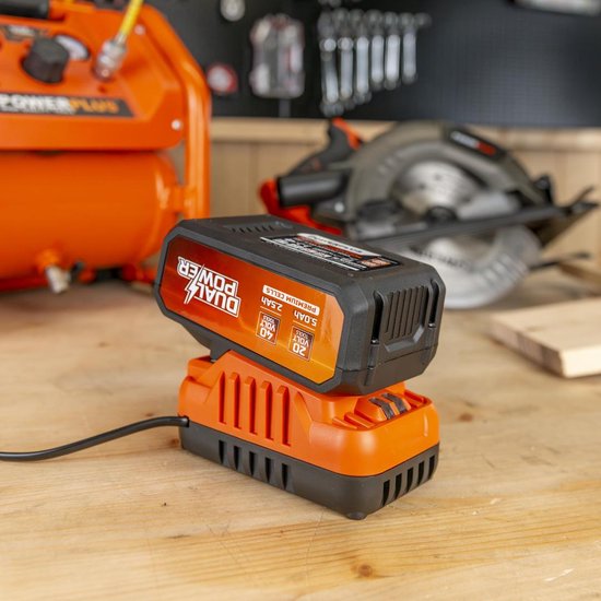 Oranje Dual Power accu op oranje lader op een houten werkbank.