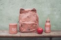 Roze rugzak met kattengezicht en stippen, naast een drinkfles en beker. Een appel ligt ervoor.