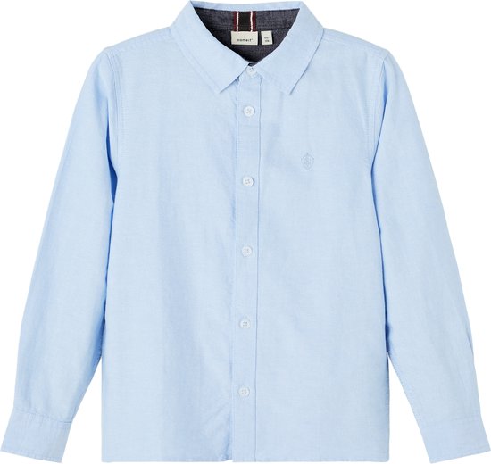Lichtblauwe katoenen jongensblouse met lange mouwen, kraag, knoopsluiting en geborduurd embleem op de borst.