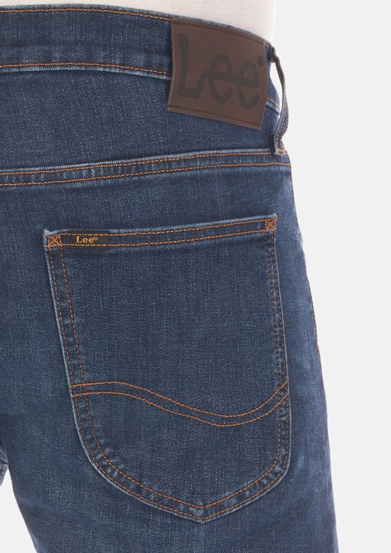 Detail van de achterzak van een donkerblauwe jeans met oranje stiksels en een bruin Lee-label.