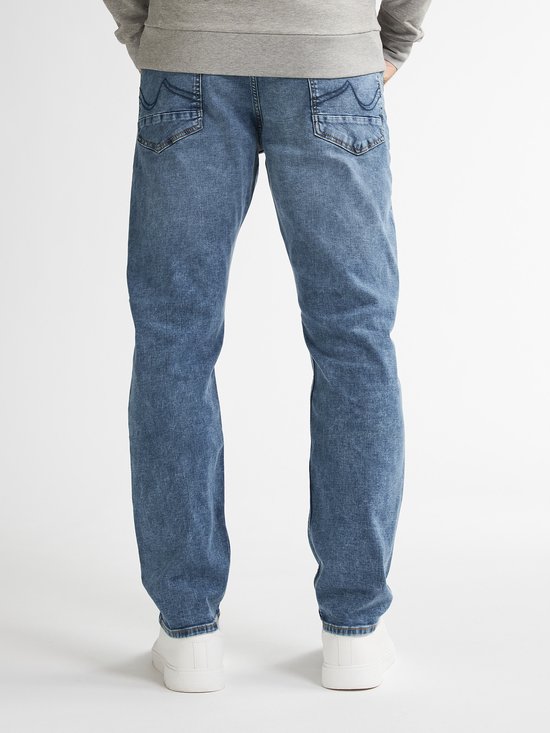 Achterkant van een man in een lichtblauwe jeans met witte sneakers. De jeans heeft decoratieve stiksels op de achterzakken.
