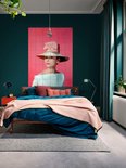 Audrey Hepburn portant un grand chapeau de paille avec un nœud rose, une robe bleu pâle épaules dénudées, sur fond rose, dans une chambre.