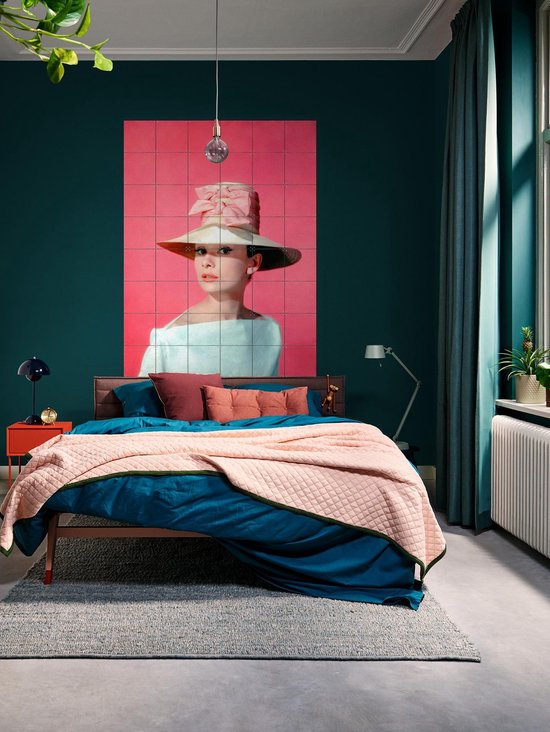 Audrey Hepburn portant un grand chapeau de paille avec un nœud rose, une robe bleu pâle épaules dénudées, sur fond rose, dans une chambre.