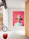 Audrey Hepburn portant un grand chapeau de paille avec un nœud rose, une robe bleu pâle épaules dénudées, sur fond rose, près d'un mur de briques.