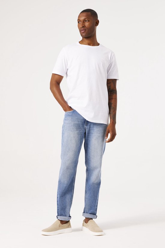 Man in een lichtblauwe jeans met casual fit, één hand in de zak.