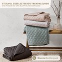 Gestapelde, gewatteerde spreien in beige, lichtgrijs en groen. Een donkergrijze sprei ligt vooraan.