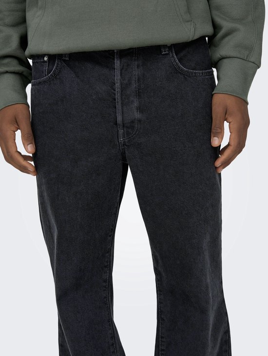 Middel en bovenbenen van een man gedragen in een wijde, zwarte spijkerbroek met stonewashed effect.