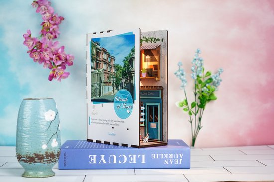 Houten boekensteun 'Island of Love' met straatafbeelding en miniatuur café, met bloemen op de achtergrond.