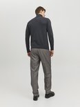 Man met de rug naar de camera, draagt een donkergrijze coltrui en een grijze pantalon met krijtstrepen.