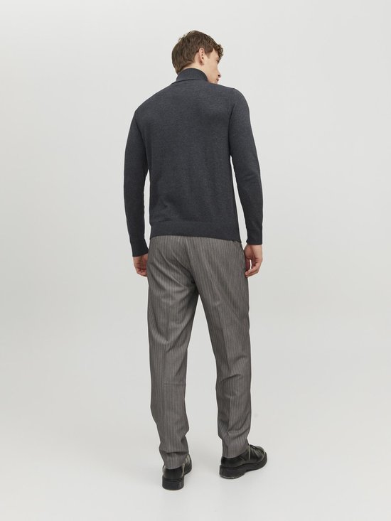 Man met de rug naar de camera, draagt een donkergrijze coltrui en een grijze pantalon met krijtstrepen.