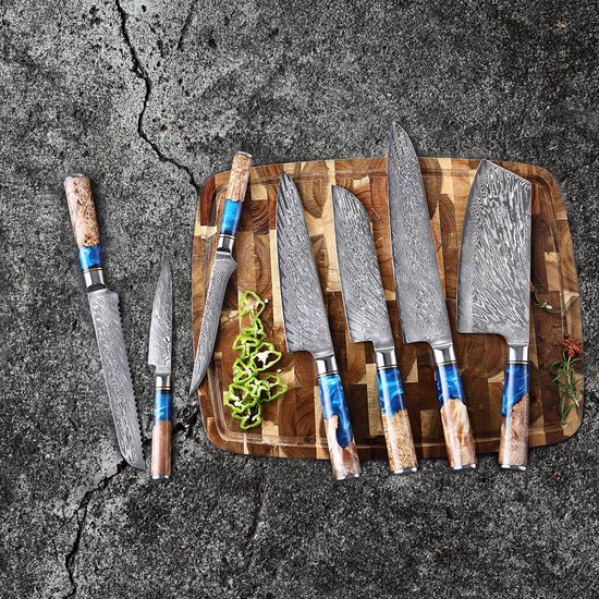 Een set van zes Damastmessensets met blauwe en bruine handvatten, gelegen op een houten snijplank met groenten.