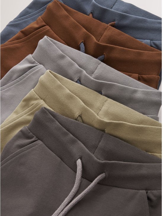 Dichtbij detail van de taillebanden van vijf joggingbroeken in grijs, beige, bruin, lichtgrijs en blauw.