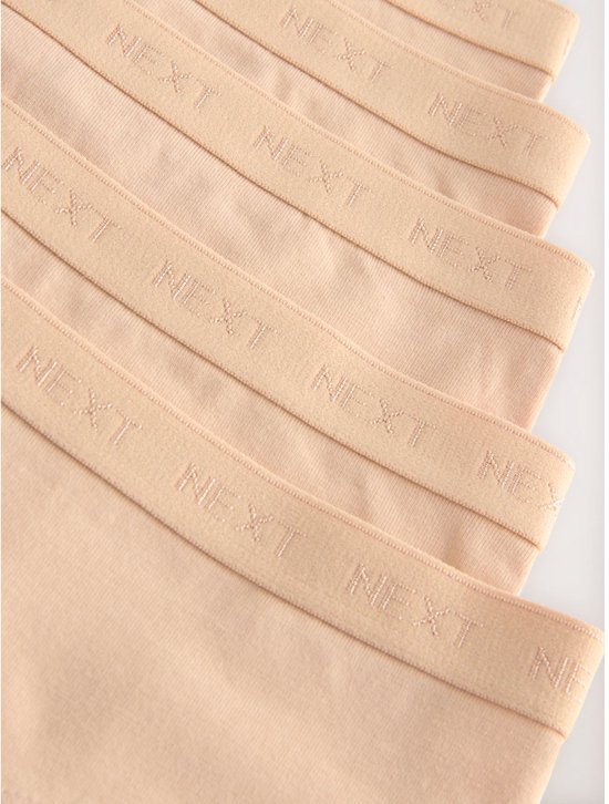 Close-up van de elastische taillebanden van beige hipsters met herhaaldelijk NEXT-logo.