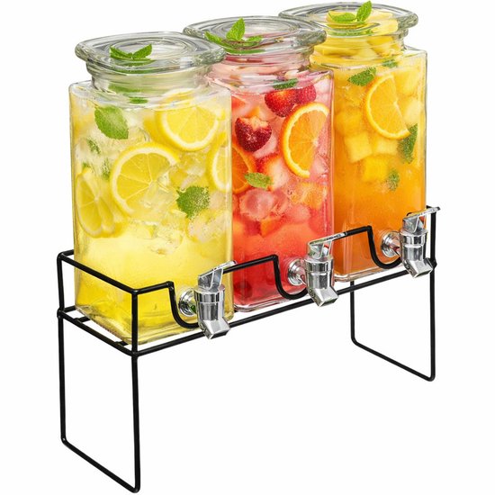 Drie glazen drankdispensers op zwarte houder, gevuld met citroen-, aardbei- en sinaasappeldrankjes met munt.