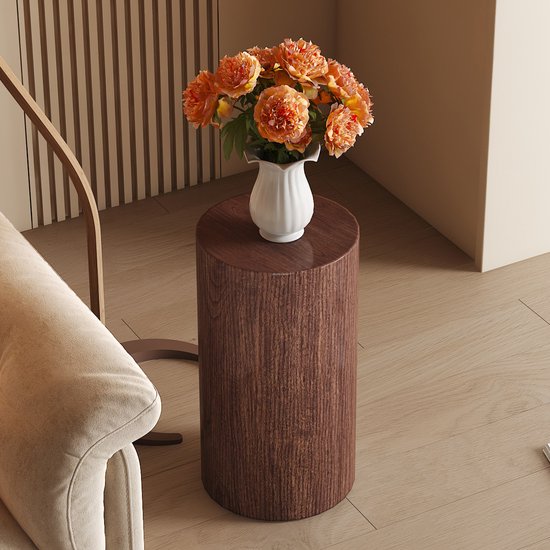 Table d'appoint ronde finition bois de noyer avec vase de fleurs oranges, à côté d'un canapé beige.