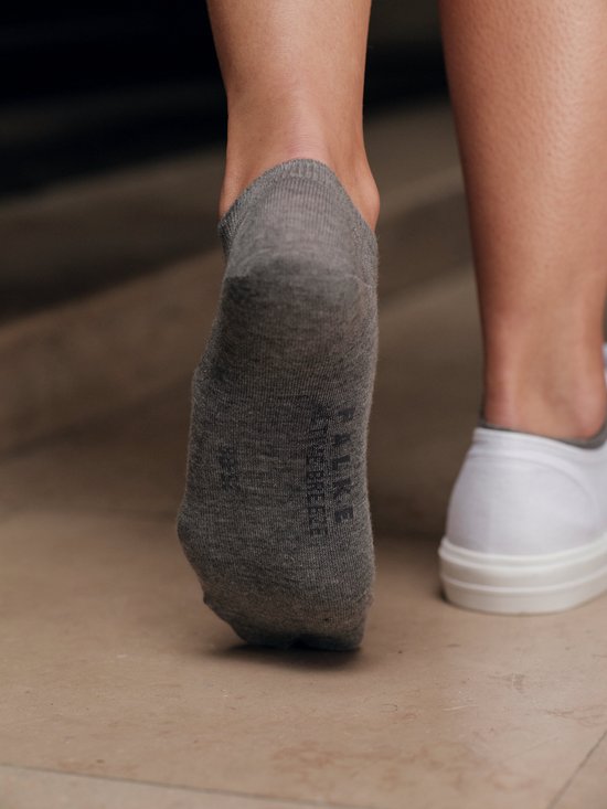 Grijze Falke sneakersokken met logo, gedragen aan de voet van een persoon met witte schoen.