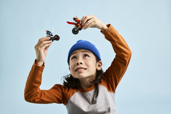 Jongen met blauwe muts houdt speelgoed ninjamotorfietsen omhoog.