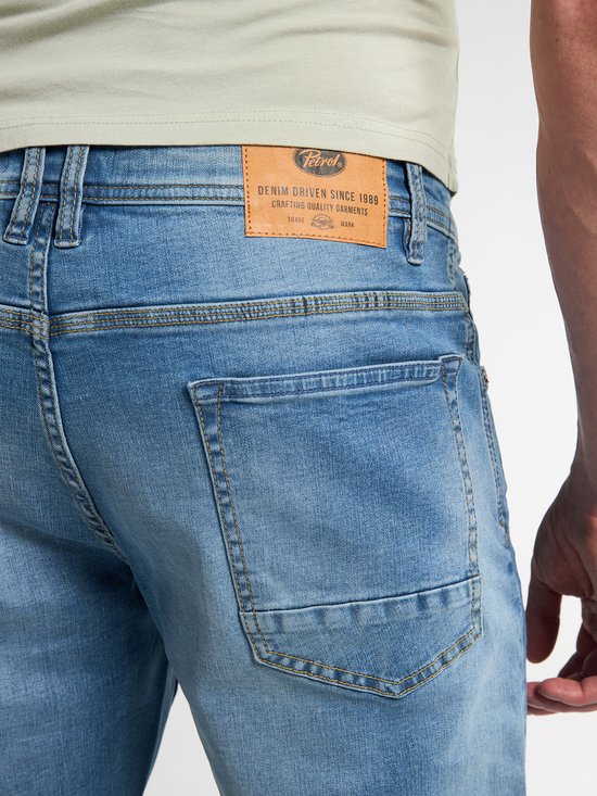 Achterzak van een lichtblauwe jeans met een leren merklabel van 'Petrol Industries'.