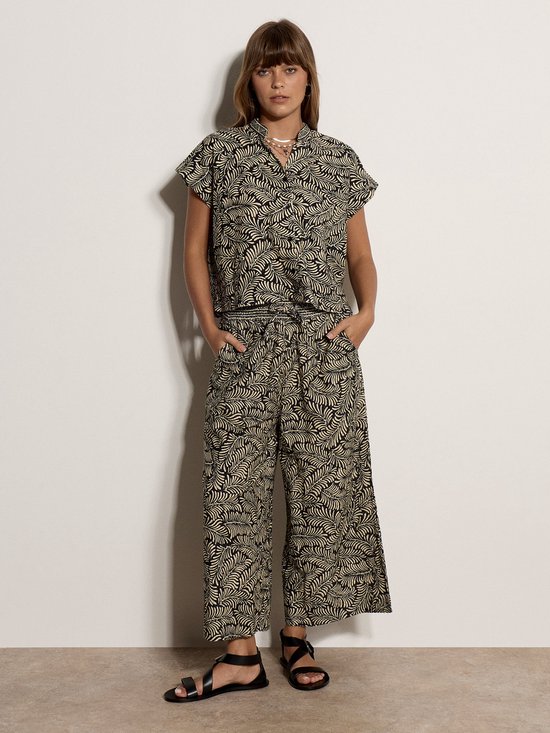 Vrouw in culotte met zwarte en beige bladprint en een bijpassend shirt met korte mouwen.