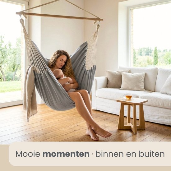 Grijze hangstoel met een vrouw en baby in een woonkamer.