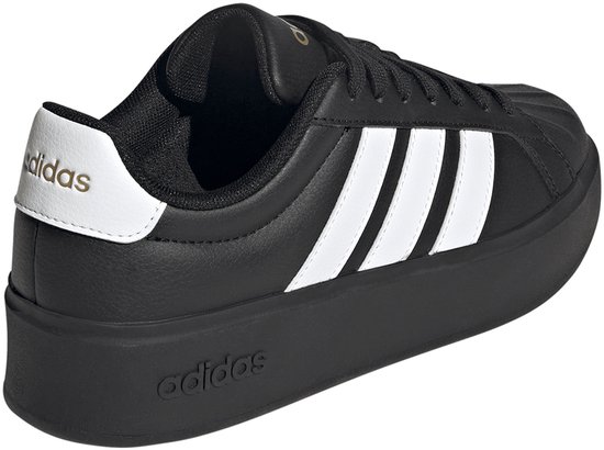 Zwarte damessneaker met dikke zool, witte Adidas-strepen op de zijkant en gouden details.