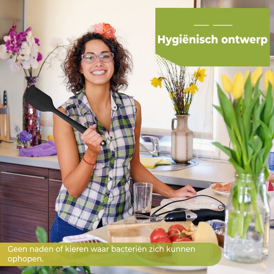 Une femme souriante portant des lunettes tient une spatule en silicone noir dans une cuisine.