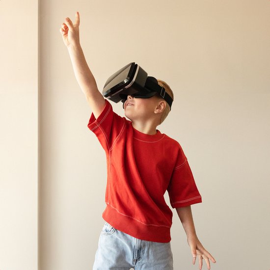 Jongen met rode T-shirt en spijkerbroek, die een VR-bril draagt en zijn arm omhoog steekt.