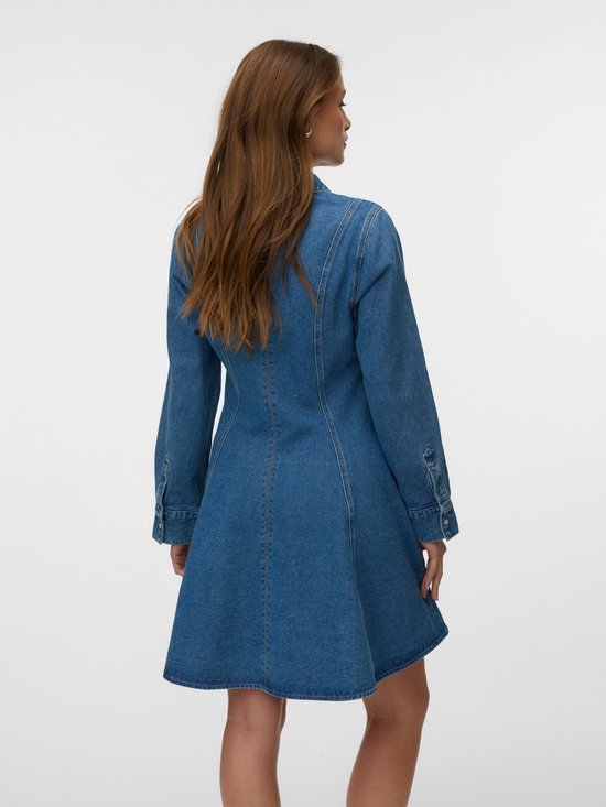 Model draagt een blauwe denim jurk met lange mouwen en een uitlopende rok, van achteren gezien.