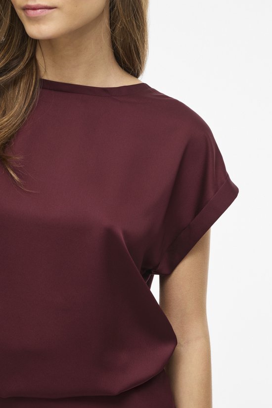 Detail van de schouder en korte, omgeslagen mouw van een bordeauxrood satijnen blouse.