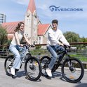 Vrolijk, jong stel in casual kleding die op witte en zwarte mountainbikes rijden, met gebouwen en bomen op de achtergrond.