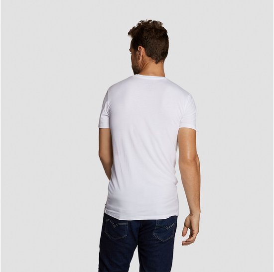 Man met donkere jeans draagt een wit, rond hals t-shirt, gezien van achteren.